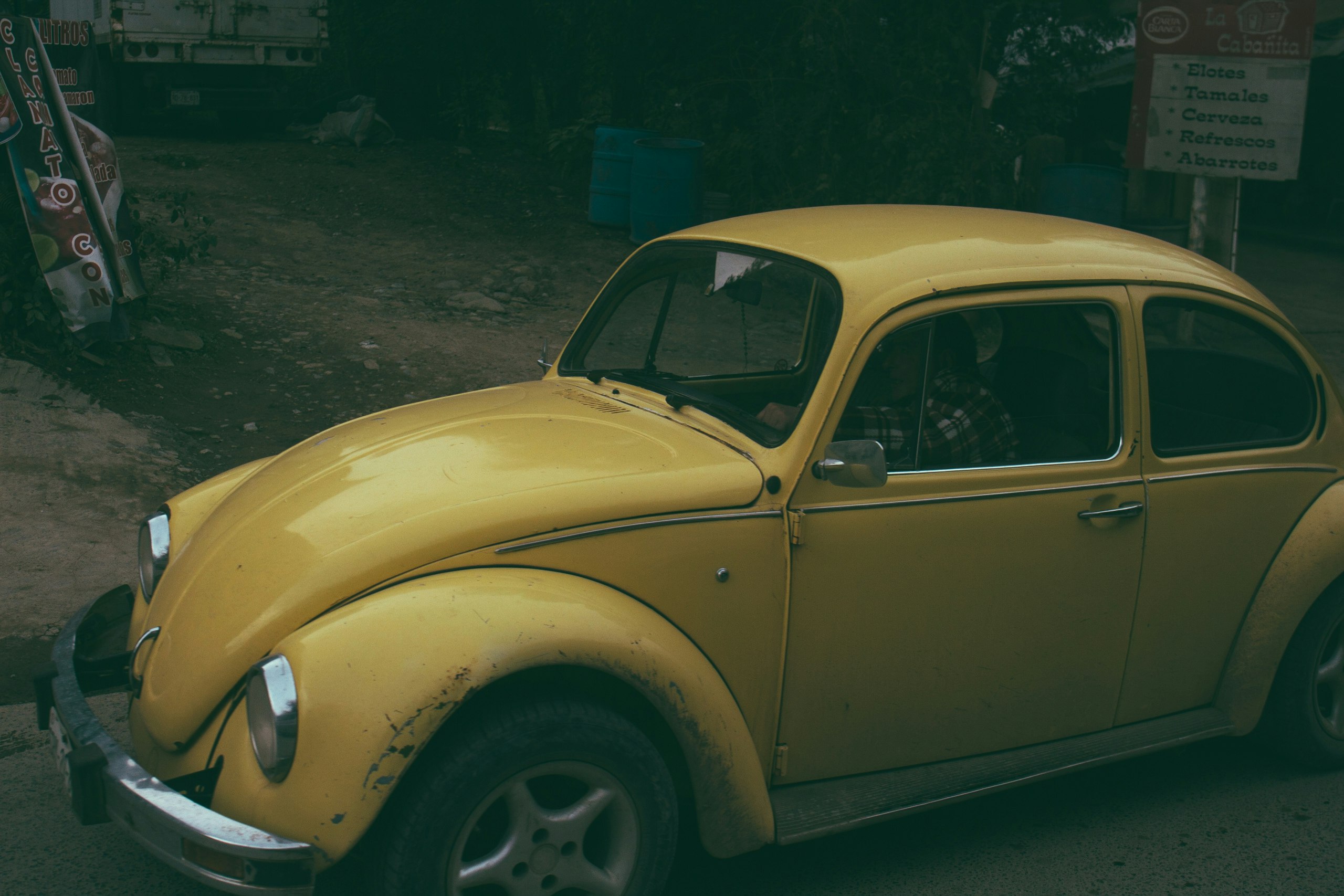 yellow Volkswagen Beetle coupe parked near white signage